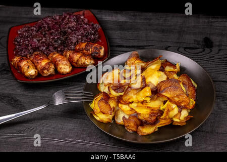 Fried potatoes and homemade grilled sausages or chevapchichi with stewed sour red cabbage on a wooden rustic background. Top view. Stock Photo