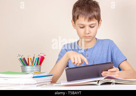 Kid sitting at table with books notebooks and using tablet computer Stock Photo