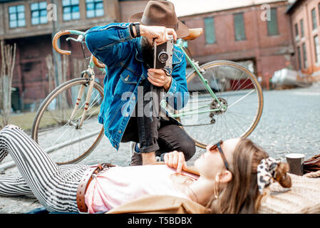 Stylish man photographing young woman lying on the street, having fun together on the urban background Stock Photo