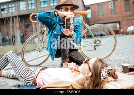 Stylish man photographing young woman lying on the street, having fun together on the urban background Stock Photo