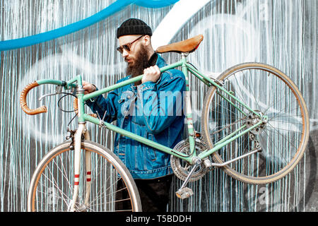 Portrait of a stylish bearded man dressed in jacket and hat with retro bicycle on the colorful wall background Stock Photo