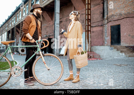 Stylish young man and woman having a conversation standing together with retro bicycle outdoors on the industrial urban background