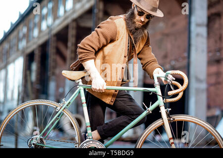 Bearded hipster dressed stylishly with hat standing with retro bicycle outdoors on the urban background Stock Photo