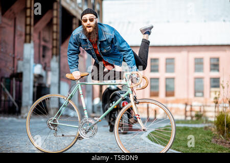 Portrait of a bearded man as a crazy hipster having fun with retro bicycle outdoors on the industrial urban background Stock Photo