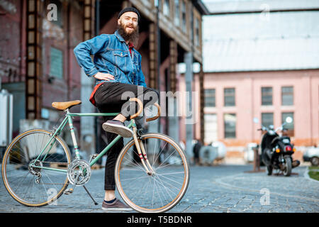 Portrait of a bearded man as a crazy hipster having fun with retro bicycle outdoors on the industrial urban background Stock Photo