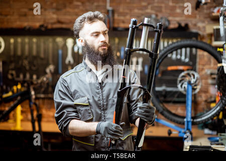 Handsome repairman holding bicycle fork while working in the beautiful bicycle workshop Stock Photo