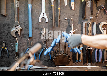 Man taking wrenches from the black wall with different tools for bicycle repairing Stock Photo