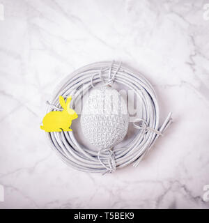 Silver easter egg and yellow easter bunny in the nest on the light marble background. Minimal concept, copy space Stock Photo