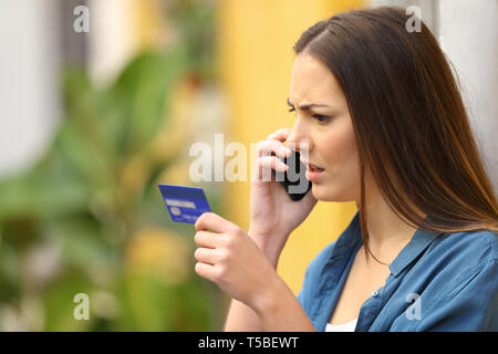 Angry online shopper complaining talking on phone holding credit card in the street Stock Photo