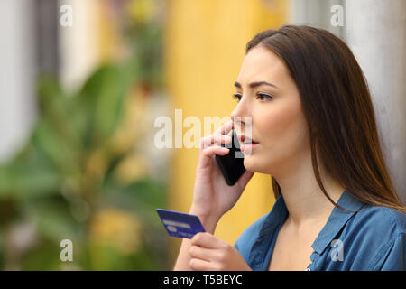 Serious buyer talking on smart phone holding credit card in the street Stock Photo
