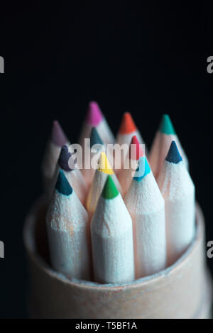 10 Coloured pencils in a pencil holder facing up, black background. Stock Photo