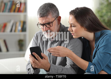 Daughter teaching how to use a phone to her mid aged father at home Stock Photo