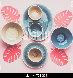 Beautiful blue, grey, beige dinnerware, plates bowls on pink table, top view, tropical leaves, toned, selective focus Stock Photo