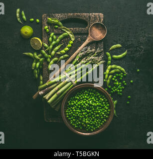 Green cooking ingredients. Green asparagus with edamame soybeans, lime and green peas on dark rustic kitchen table background, top view.  Healthy vege Stock Photo