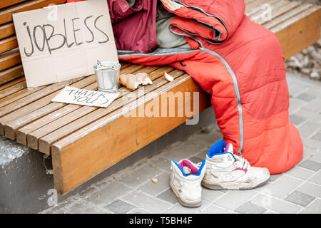 Jobless beggar with cardboard and cup begging some money, close-up view with no face Stock Photo