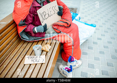Jobless beggar with cardboard and cup begging some money, close-up view with no face Stock Photo
