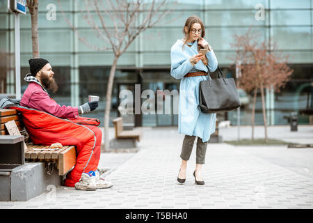 Homeless begging money while sitting on the bench with passing by businesswoman near the business center Stock Photo