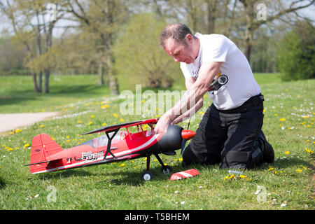 Close up of man in country park (the controller) kneeling on grass, fixing receiver/making adjustments to his radio-controlled, flying model aircraft. Stock Photo