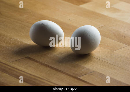 two white eggs laying on a wooden kitchen worktop Stock Photo