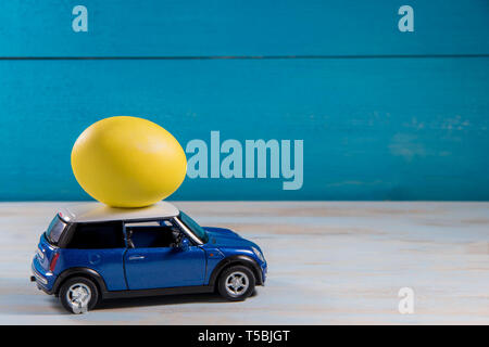 Yellow Easter egg in blue toy car with white roof on a blue background Stock Photo
