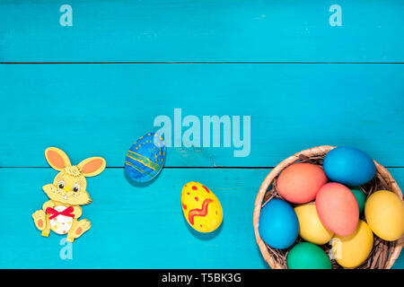 Easter bunny next to easter eggs on a blue wooden background next to basket with color easter eggs Stock Photo