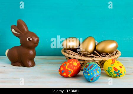 Delicious chocolate Easter rabbit next to Easter eggs in basket on blue wooden background with copyspace Stock Photo