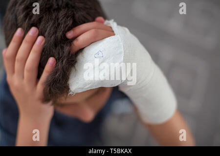 Boy with broken arm touching head Stock Photo