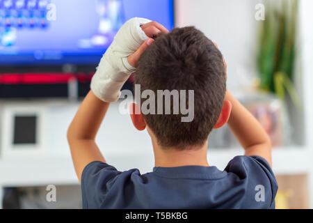 Anonymous boy with broken arm watching TV Stock Photo