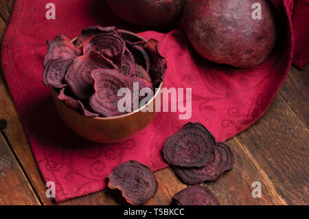 Beetroot chips in wooden bowl and whole beetroots on red napkin on old wooden table.  Stock Photo