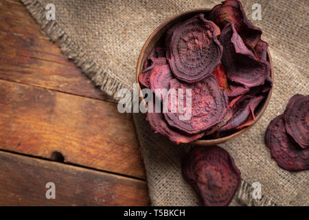 Beetroot chips in wooden bowl on burlap napkin on old wooden table.  Stock Photo