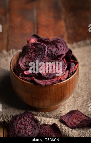 Close-up healthy beetroot chips in wooden bowl on burlap napkin on old wooden table. Stock Photo