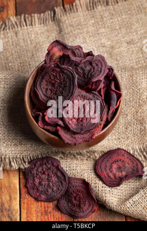 Top view beetroot chips in wooden bowl on burlap napkin on old wooden table. Stock Photo
