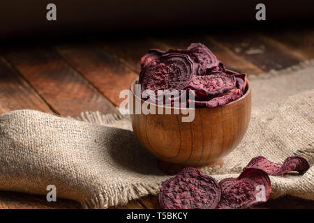 Beetroot chips in wooden bowl on burlap on wooden table on dark background. Stock Photo