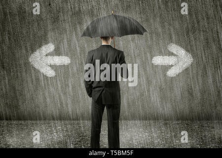 confused businessman is standing in front of a wall on a gloomy day and has to make a decision - which way left or right Stock Photo