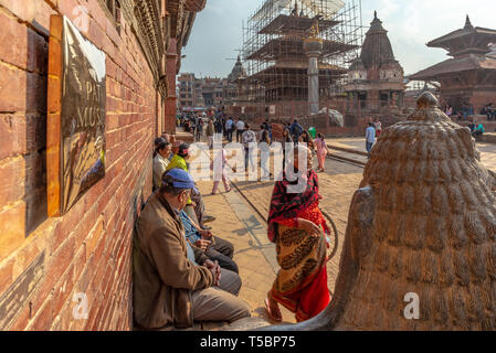 LALITPUR, PATAN, NEPAL - APRIL 3, 2019: Head of a lion guard, crowd and indian woman walking, next to the Royal Palace Stock Photo