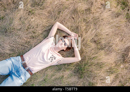 Young woman on the grass appreciates the spring. Top view of a relaxed female person laying in the meadow or field an looking at the sky Stock Photo