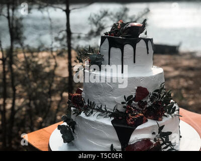 Beautiful three-tiered white cream wedding cake with pomegranate fruit and fresh flowers Stock Photo