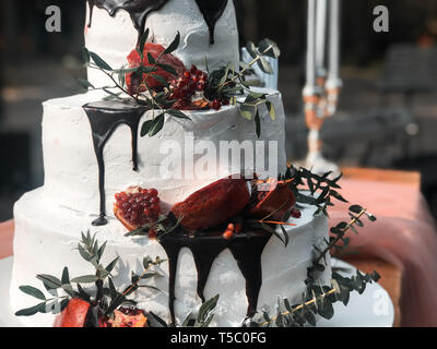 Beautiful three-tiered white cream wedding cake with pomegranate fruit and fresh flowers Stock Photo