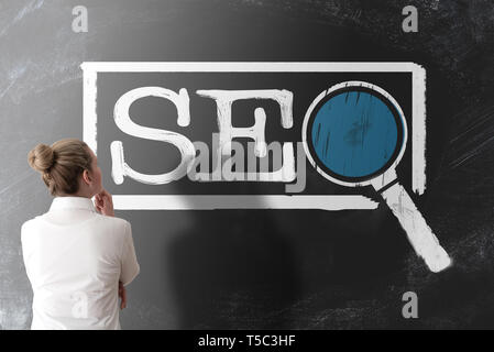 rear view of woman in white blouse looking at term SEO, search engine optimization,  on chalkboard Stock Photo