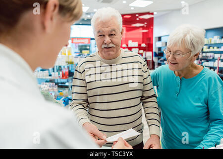 Pharmacist getting prescription slip from senior couple Stock Photo