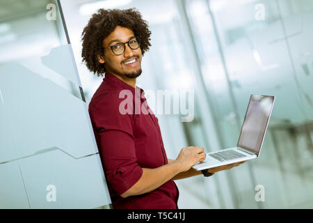 Happy young handsome African American IT specialist wearing glasses working on his laptop in the office Stock Photo