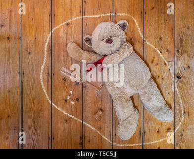Teddy bear lying on floor with an empty glass, pills and chalk outline. Concept. Stock Photo
