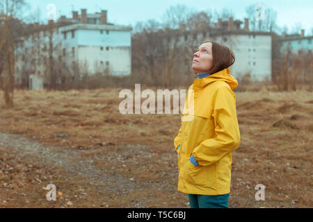 Woman in yellow raincoat looking up at rainy clouds while the raindrops are falling on her face Stock Photo