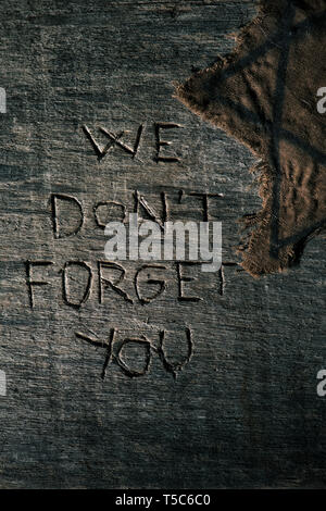high angle view of a ragged jewish badge on a gray rustic wooden surface with the text we dont forget you carved in it Stock Photo