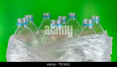 Bottlenecks of a pack of 8 empty and recyclable plastic water bottles, with no caps, blue seal, inside a plastic bag, on a colored vivid green Stock Photo