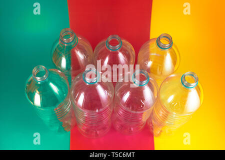 A pack of 7 empty and recyclable plastic water bottles, with no caps, blue seal, on a colored vibrant sea green, wine red, and yellow background Stock Photo