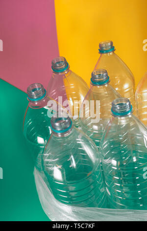 A pack of 7 empty and recyclable plastic water bottles, with no caps, blue seal, in a plastic bag, on a colored pastel tones of sea green, soft pink Stock Photo