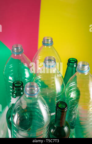 Sets of empty glass bottles and plastic bottles with no label on a vivid green, wine red and yellow colored background. Reuse, Eco-Friendly Stock Photo