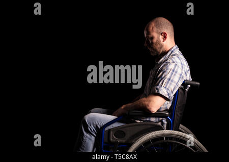 Portrait of caucasian man sitting in a wheelchair, sad and thoughtful expression. Black background. Concept of patient and physical disability. Stock Photo