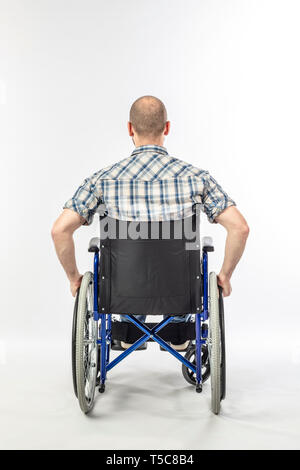 Man sitting on a wheelchair because he is injured. white background and back view. Concept of disability and medical support. Stock Photo